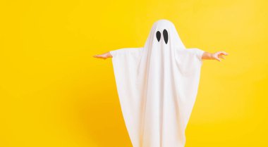 Komik cadılar bayramı çocuğu kavramı, yakın plan beyaz kostümlü küçük şirin çocuk cadılar bayramı hayaleti korkunç, sarı arka planda izole edilmiş stüdyo resmi.