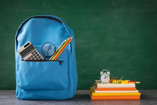 Front of stylish school bag backpack and stationery accessory on a table desk at the green chalkboard, Back to school education concept