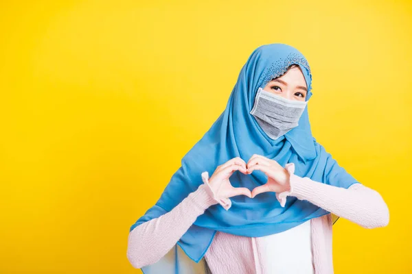 アジアのイスラム教徒アラブ 幸せな美しい若い女性の肖像イスラム教の宗教的な摩耗ベールヒジャーブと顔のマスクは 隔離された黄色の指の心の図を手の病気のコロナウイルスを示しています — ストック写真