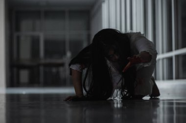 Korkunç kötü kadın hayalet sürünen sürüngen evdeki karanlık bir odada yavaşça sürünüyor. Kan içindeki dişi zombi korkunçtur. Terk edilmiş binaya dadandı. Mutlu Cadılar Bayramı festivali konsepti.