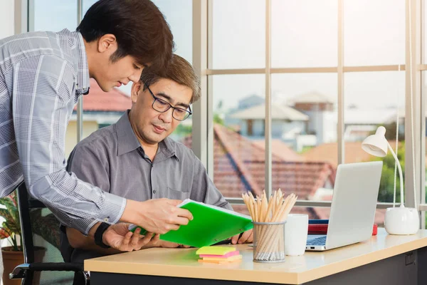 Asian senior and junior two businessmen discuss something during their meeting consultation project, Mature boss with a business partner working together on the laptop computer on desk home office