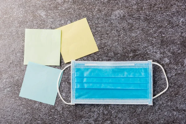 Above blank paper stick note list yellow, green and blue with the face mask protective on concrete background, Quarantines disease coronavirus or COVID-19 and write note stick memory work today