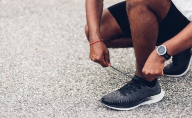 Kapatın Asyalı spor koşucusu siyah adam kol saati takıyor ayakkabı bağcığı deniyor koşuya hazırlanıyor ve sağlık parkında koşuyor, sağlıklı egzersiz konsepti.
