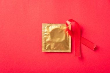 Kırmızı kurdele HIV, AIDS kanseri farkındalığı ve gölgeli prezervatif, kırmızı arka planda izole edilmiş stüdyo çekimi, sağlık sigortası cinsel konsepti, Dünya AIDS Günü