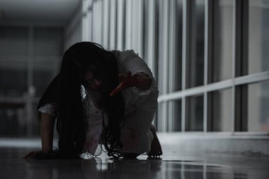 Korkunç kötü kadın hayalet sürünen sürüngen evdeki karanlık bir odada yavaşça sürünüyor. Kan içindeki dişi zombi korkunçtur. Terk edilmiş binaya dadandı. Mutlu Cadılar Bayramı festivali konsepti.