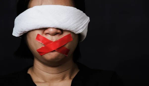 Slave Asian woman blindfold wrapping mouth with red adhesive tape, tied with chains and closed her eyes black background. Freedom speech censorship and stop talk, International Human Rights day