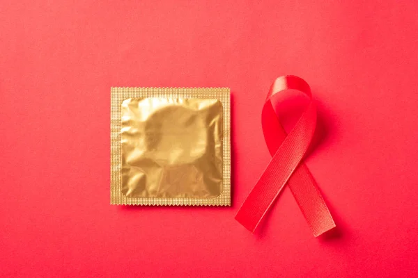 Red bow ribbon symbol HIV, AIDS cancer awareness and condom with shadows, studio shot isolated on red background, Healthcare medicine sexually concept, World AIDS Day