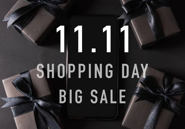 11:11 sale shopping concept, Top view of gift box wrapped black paper and black bow ribbon present around a smartphone with 11.11 shopping and big sale text, studio shot on dark background