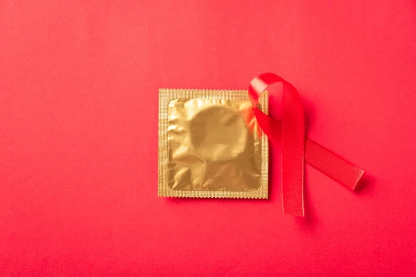 Red bow ribbon symbol HIV, AIDS cancer awareness and condom with shadows, studio shot isolated on red background, Healthcare medicine sexually concept, World AIDS Day