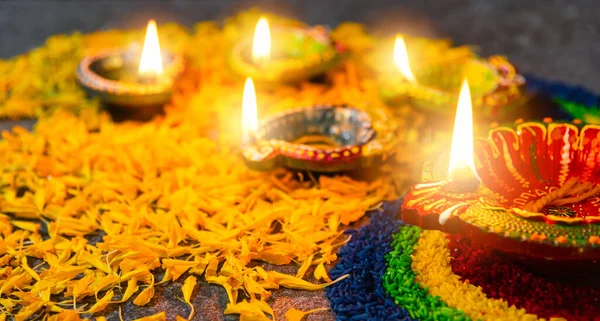 Close up clay lit light a fire already on Diya or oil lamp with flowers on concrete background, Decoration of Hinduism rangoli, Happy celebration Deepavali, or Diwali Indian festival concept