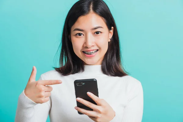 美しいアジアの女性の笑顔彼女はスマートフォンに指を指して 青い背景に隔離された携帯電話で彼女のポイント指を昇進を受け取った後 女性は陽気に興奮 技術の概念 — ストック写真