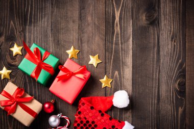 Noel dekorasyonu hazır. Noel Baba şapkası, yıldız, süs ve Noel hediyesi kutusunun düz manzarası siyah ahşap arka planda fotokopi alanı ve yeni yıl kartı konseptiyle yatıyordu.