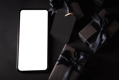 Kara Cuma alışverişi konsepti, hediye kutusunun üst görüntüsü siyah kağıt ve siyah kurdele sarılı akıllı telefon boş ekran, karanlık arka planda stüdyo çekimi