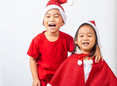 Asyalı küçük sevimli iki kardeş, erkek ve kız kardeş, kırmızı Noel Baba şapkası takmış, Noel tatili konseptini kucaklayan çocuklar ya da yeni yılınız kutlu olsun, beyaz arka planda izole edilmiş.