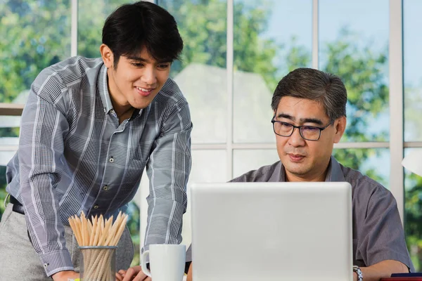Asian senior and junior two businessmen discuss something during their meeting consultation project, Mature boss with a business partner working together on the laptop computer on desk home office