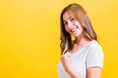 Asya 'nın mutlu portresi güzel genç kadın tişörtü giyiyor. Kazanan yumruklarını kaldırıyor. Kameraya bakıyor, izole edilmiş sarı arka planda fotokopi çekiyor.