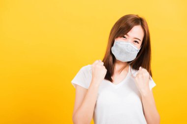 Yüz maskesi takan Asyalı güzel güzel bir kadın filtre tozu pm2.5, virüs ve hava kirliliğini koruyor. Sarı arka planda hastalıktan kurtulduktan sonra sevinçten havalara uçuyor.