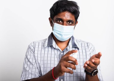 Gözlerinde koruyucu yüz maskesi olan Asyalı siyah adam, beyaz arka planda izole edilmiş dezenfektan spreyi, hijyen önleme COVID-19 virüsü veya koronavirüs koruma kavramı gösteriyor.