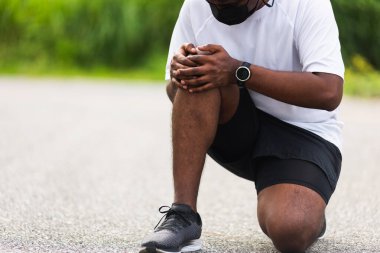 Kapatın Asyalı genç spor koşucusu. Siyah adam, el ele oturuyor. Açık hava sokak sağlık parkında koşarken diz ağrısı çekiyor.