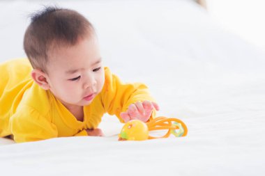 Yeni doğmuş güzel Asyalı bebeğin portresi evde yatağında yatar mutlu bebek gülüşü odada dinlenen sarı bir gömlek giyer aile sabahı evde dinlenir.