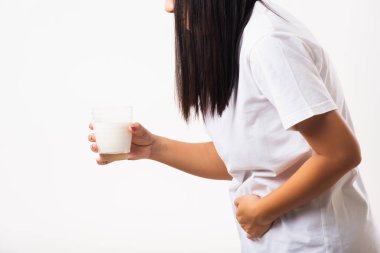 Yakından genç bir kadın hoşgörüsüz, cam sütle el ele tutuşuyor, midesi ağrıyor, laktoza dayanıksızlığı var süt ürünleriyle ilgili sağlıksız bir sorunu var, beyaz arka planda izole edilmiş bir stüdyo çekimi.