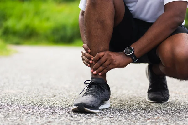 在室外街道健康公园跑步时扭伤脚踝 造成健康的运动损伤 亚洲年轻的运动健将黑衣人戴着手表 手关节紧紧抓住腿疼 — 图库照片