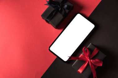 Kara Cuma alışveriş konsepti, siyah kurdele ve siyah kurdeleye sarılı hediye kutusu manzarası ve modern cep telefonu, kırmızı ve koyu arkaplan üzerine stüdyo çekimi.