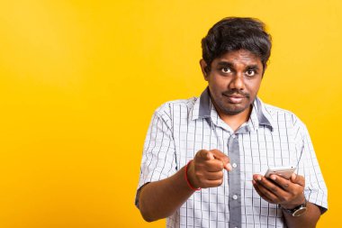 Yakın plan Asyalı mutlu portre genç zenci bir cep telefonu tutuyor ve kamerayı işaret ediyor. Stüdyo sarı arka planda izole edilmiş.