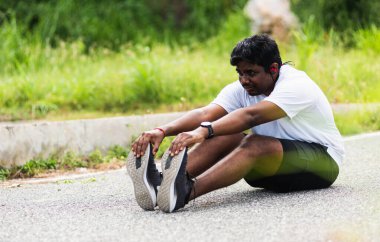 Kapatın Asyalı genç sporcu spor koşucusu siyah adam kol saati takıyor ayak parmaklarını uzatıyor bacaklarını ve dizlerini esnetiyor açık hava parkına koşmadan önce spor konseptinden önce sağlıklı egzersiz.