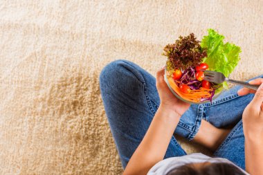 Bacağında yeşil marul salatası olan kadın ellerinin üst görüntüsü, taze salata yiyen genç bir kadın kasede vejetaryen ıspanak yiyor, sağlıklı gıda konseptini temizliyor.