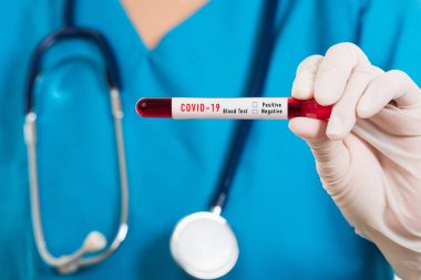 Mavi üniformalı hemşire laboratuarda beyaz arka planda izole edilmiş Coronavirus test kanını, COVID-19 ilaç salgın konseptini incelemek için bir maske takıyor.