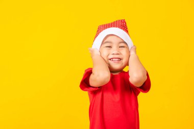 Küçük çocuk gülümsüyor ve heyecanlanıyor, kırmızı Noel Baba şapkası takmış çocuklar el ele tutuşup, Noel tatili konseptini kucaklıyor ya da sarı arka planda izole edilmiş yeni yılınız kutlu olsun.