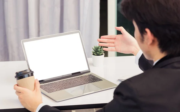 Work from home, Asian young businessman smile wearing suit video conference call or facetime by laptop computer raise his hand to explain to teammates on desk at home office