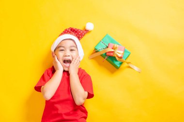 Asyalı küçük sevimli çocuk gülümsüyor, Noel Baba kılıklı bir çocuğun en iyi görüntüsü Noel tatili şapkası ya da yeni yıl noeli konsepti sarı arka planda izole bir şekilde yatıyor.
