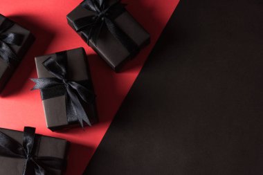 Kara Cuma alışveriş konsepti, siyah kağıt ve siyah kurdeleye sarılı hediye kutusu manzarası, kırmızı ve koyu arka planda izole edilmiş stüdyo çekimi.