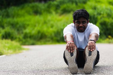 Kapatın Asyalı genç sporcu spor koşucusu siyah adam kol saati takıyor ayak parmaklarını uzatıyor bacaklarını ve dizlerini esnetiyor açık hava parkına koşmadan önce spor konseptinden önce sağlıklı egzersiz.