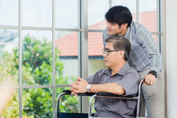 車椅子のアジアの高齢者障害者のビジネスマンは オフィスのチームとの交流について話し合う 車椅子の老人と幼い息子が父と話をして慰めました — ストック写真