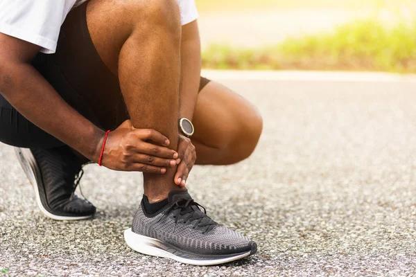 在室外街道健康公园跑步时扭伤脚踝 造成健康的运动损伤 亚洲年轻的运动健将黑衣人戴着手表 手关节紧紧抓住腿疼 — 图库照片