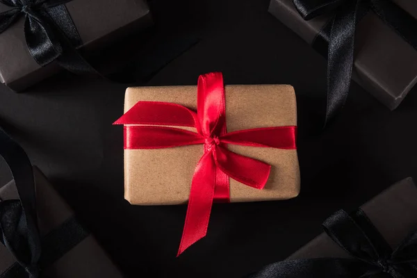 黑色星期五购物理念 礼品盒顶部的包装纸和黑色蝴蝶结带周围的棕色盒子与红色蝴蝶结带 工作室拍摄黑色背景 — 图库照片