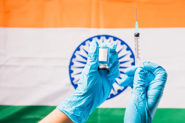 Hands of doctor wear gloves holding coronavirus (COVID-19) vial vaccine and syringe on flag India background, India Vaccination