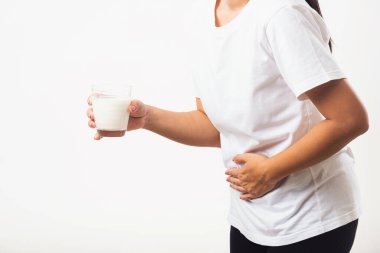 Yakından genç bir kadın hoşgörüsüz, cam sütle el ele tutuşuyor, midesi ağrıyor, laktoza dayanıksızlığı var süt ürünleriyle ilgili sağlıksız bir sorunu var, beyaz arka planda izole edilmiş bir stüdyo çekimi.