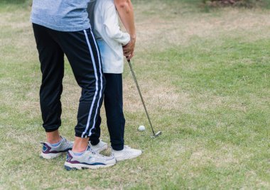 Asyalı genç baba, mükemmel golf oynamayı öğretirken aynı zamanda doğada birlikte golf oynamayı öğretiyor. Bir saha bahçesi parkı, aile spor kavramı.