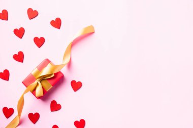 Sevgililer Günü kompozisyon konseptin kutlu olsun. Altın kurdeleli kırmızı hediye kutusu ve pembe arka planda izole edilmiş aşk için ahşap kırmızı kalpler fotokopi alanı. Yukarıdan Üst Görünüm