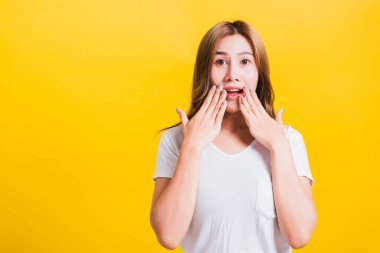 Asya 'nın mutlu portresi. Güzel, şirin, şaşkın, şaşkın, ağzı açık, el hareketleriyle kameraya bakan, sarı arka planda izole edilmiş, fotokopi alanı ile izole edilmiş bir stüdyo resmi.