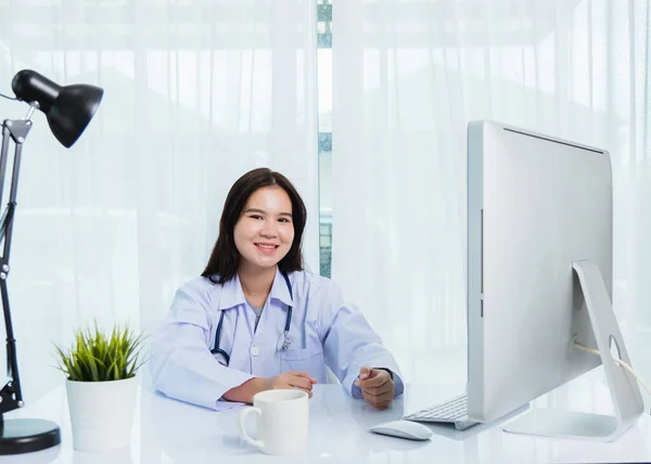 アジアの若い美しい女性医師ビデオ通話会議オンライン座ってフロントデスクトップPcのモニター検疫疾患コロナウイルスや病院のオフィスでCovid 19について説明する患者を聞きます — ストック写真