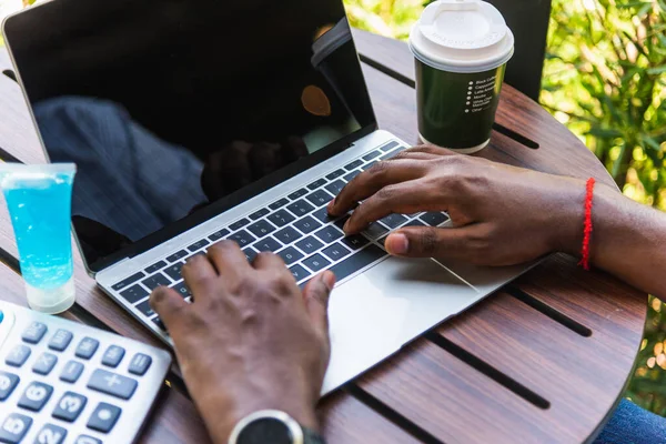 Happy Asian black businessman person or office worker wear face mask protect sitting on desk work from home using laptop computer typing keyboard and connect networking online at the coffee cafe shop