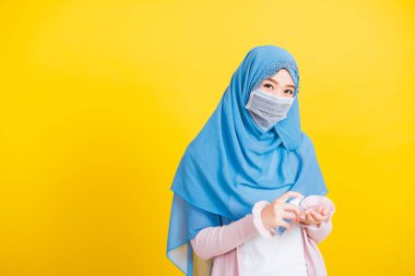 Asyalı Müslüman Arap, mutlu genç kadın portresi İslam dini peçe takıyor ve yüz maskesi takıyor hastalık koronavirüsü karantinaya alıyor izole edilmiş sarı ellere alkol spreyi sıkıyor