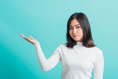 Genç, güzel, Asyalı bir kadın makyaj malzemeleri gösterirken gülümsüyor, portre kadın elinde bir şey sunuyor, stüdyo çekimi mavi arka planda izole edilmiş.