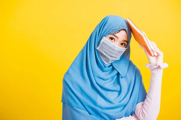アジア系ムスリムアラブ人 若い女性の肖像宗教的な摩耗ベールヒジャーブと顔のマスク保護彼女は学生が手に本を保持するコロナウイルスを防ぐために 黄色の背景に孤立 大学に戻る — ストック写真