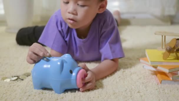 快乐的亚洲男孩幼儿园把别针钱币放入蓝脸小猪槽 小孩子把硬币放在储蓄罐里 以便在家里堆放硬币存钱 — 图库视频影像